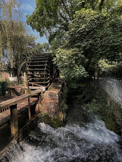 Old wooden water mill wheel on a stream with flowing water, green trees, and stone walls
