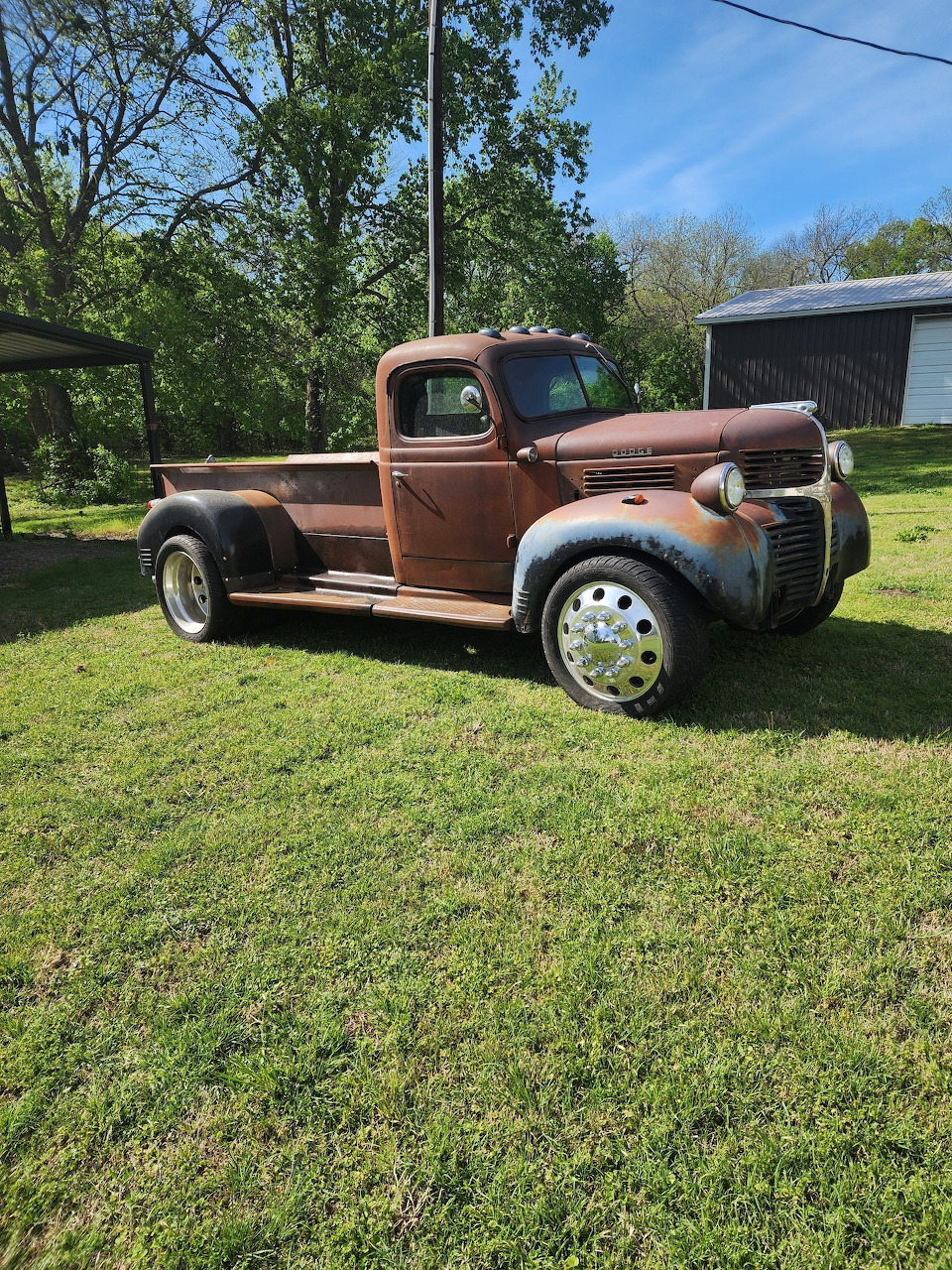 Rusty vintage 1940s pickup truck parked on green lawn with trees in background