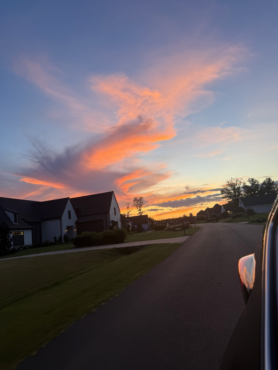 Colorful orange and pink sunset clouds over a suburban neighborhood street with houses silhouetted