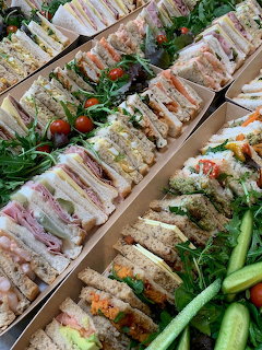 Assorted sandwich platters with triangle sandwiches, greens, cucumbers, and cherry tomatoes