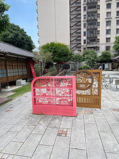 Pink and brown ornate decorative panels on a paved plaza with traditional buildings and skyscrapers in Zhongli, Taiwan