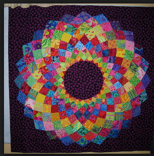 Colorful patchwork quilt with flower mandala pattern in rainbow fabrics on dark purple polka dot background