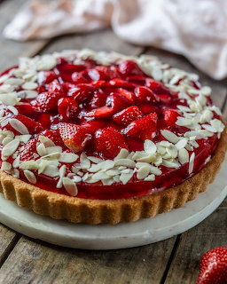 Round strawberry tart with custard filling and sliced almonds on white plate