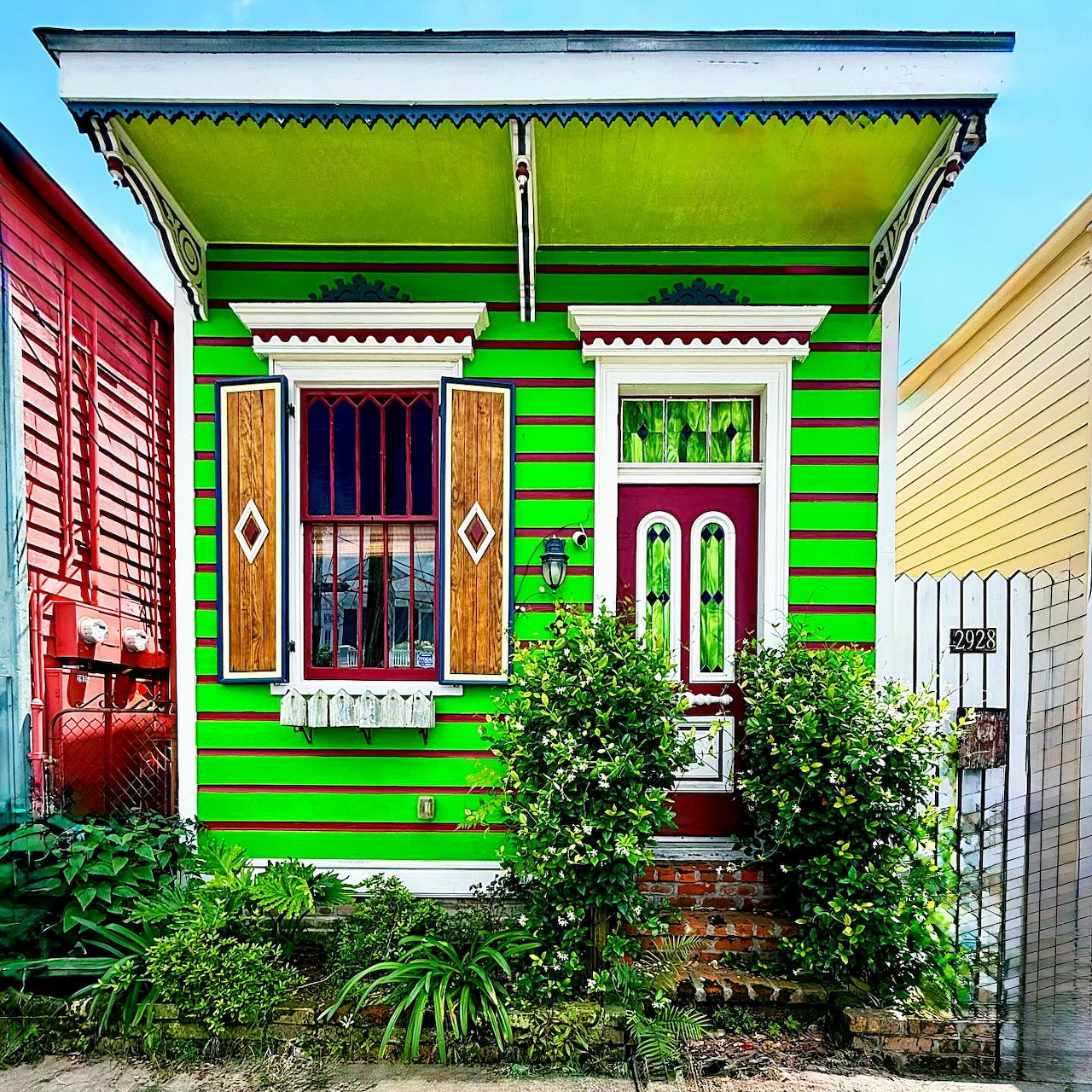 Bright lime green Victorian cottage with white decorative trim, colorful door and windows, front garden and brick steps