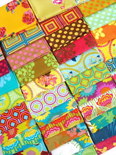Colorful patchwork quilt with various fabric patterns in rainbow colors including florals, dots, and geometric designs