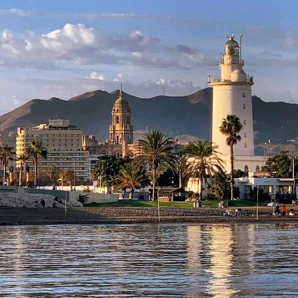 Coastal city waterfront with white lighthouse, palm trees, and mountain backdrop