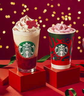 Two festive whipped tea drinks on red gift boxes with golden lights in the background.