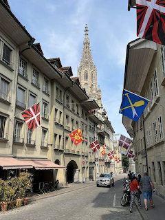 Cobblestone street in Bern with sandstone buildings, hanging flags, and cathedral tower in distance