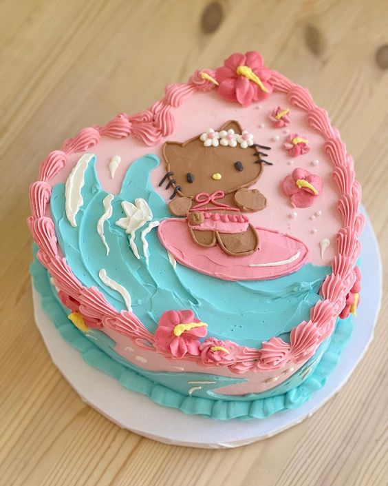 Heart-shaped Hello Kitty cake with pink and turquoise frosting and surfing character decoration