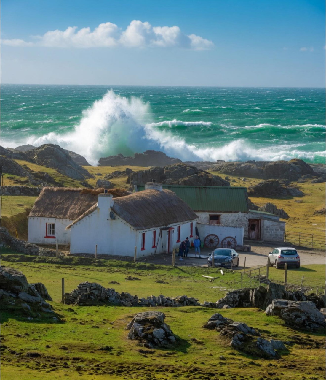 White coastal cottages on grassy rocks with large ocean waves crashing behind them