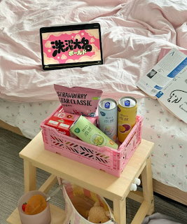 Pink snack tray on a small table beside an unmade bed with a tablet on the blanket