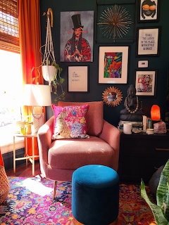 Eclectic living room with pink chair, teal wall, framed art, and colorful decor