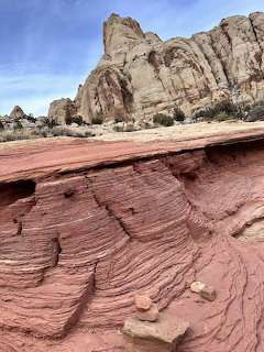 Red layered sandstone in foreground with white cliff formations and blue sky at Capitol Reef National Park