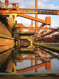 Orange rusty industrial buildings and pipes of Zollverein coal mine reflected in water