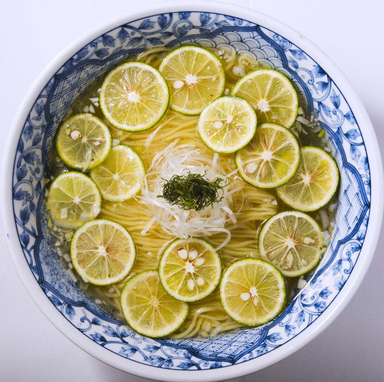 Top view of ramen in a blue patterned bowl topped with sliced green citrus