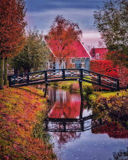 Wooden footbridge over a canal with autumn trees and a Dutch house reflected in still water
