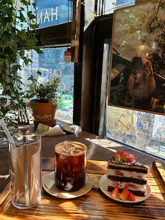 Cafe table with iced coffee and chocolate cake near a sunlit window with green plants