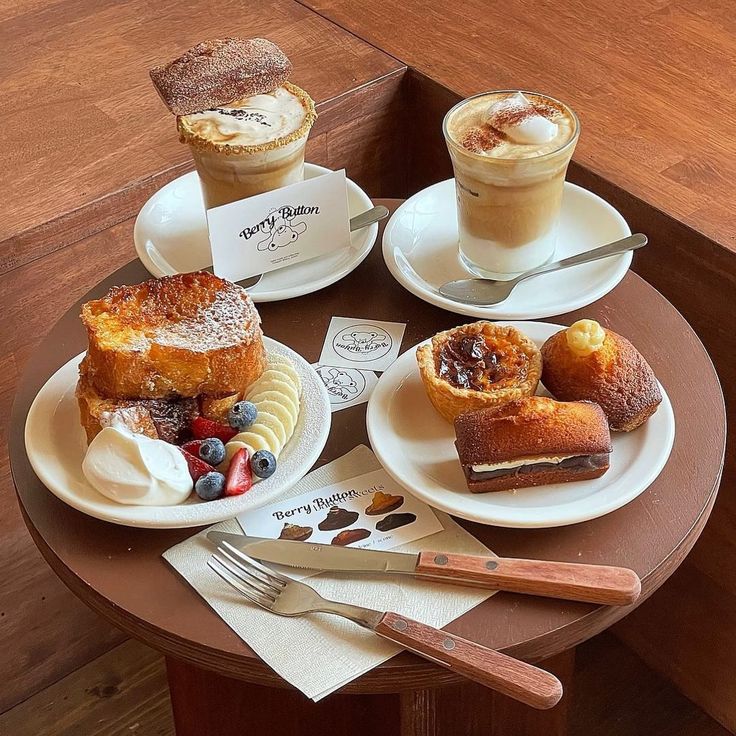 Two lattes and assorted breakfast pastries on plates arranged on a brown wooden tray