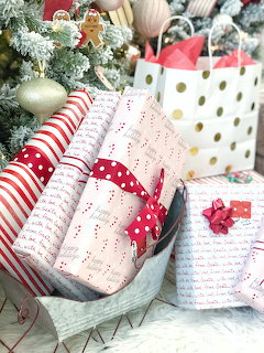 Wrapped Christmas gift boxes with red ribbons beside a decorated tree and colorful gift bags