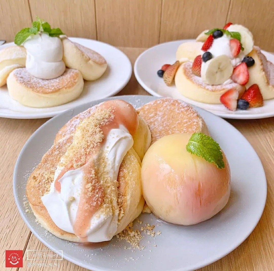 Three plates of fluffy Japanese soufflé pancakes with whipped cream, peach, and berry toppings on a wooden table