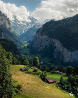 Swiss alpine valley with green meadows, wooden chalets, steep cliffs, and snow-capped mountains