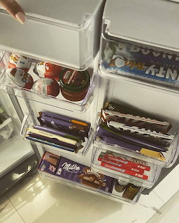 Open fridge with multiple clear drawers filled with chocolate bars and candy organized neatly