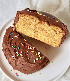 Slice of yellow cake with chocolate frosting and rainbow sprinkles on a white plate