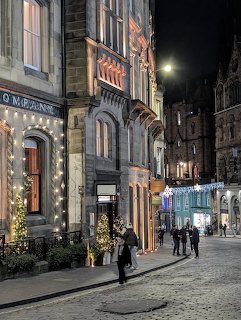 Historic city street at night with lit buildings, cobblestones, and a few pedestrians
