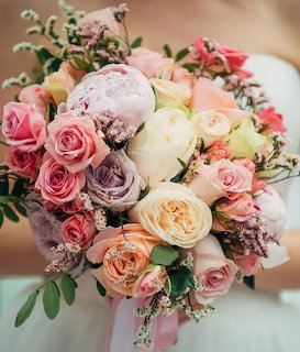 Colorful bridal bouquet with pink, peach, white and lavender roses held by a bride
