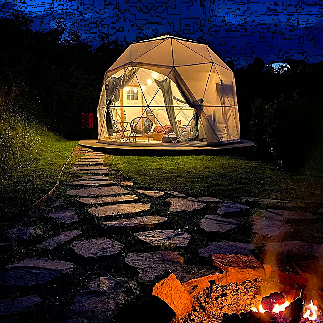 Lit geodesic dome tent at night with campfire and stone path in twilight setting