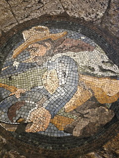 Ancient Roman mosaic of a fish made from small colored stone tiles in circular frame