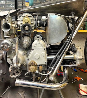 Vintage motorcycle engine with chrome exhaust pipes and fuel tank on workshop stand