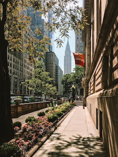 Sunny city street with flowering plants, trees, and Empire State Building in distance