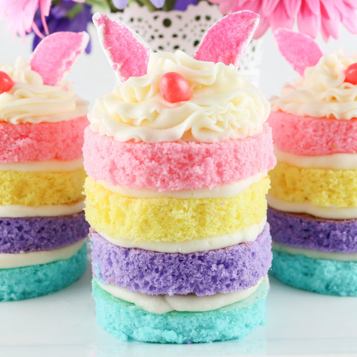 Stacked rainbow layer cakes with white frosting and pink butterfly toppers