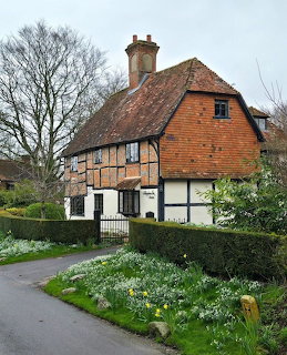 Tudor-style cottage with timber framing, tile roof, and garden of white spring flowers