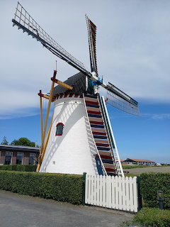 White Dutch windmill with colorful striped blades against a blue sky, white fence and green hedge in foreground