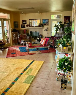 Colorful eclectic living room with vibrant rugs, patterned furniture, plants, and art on yellow walls