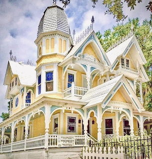 Victorian yellow house with white trim, porch, and turret behind an iron fence