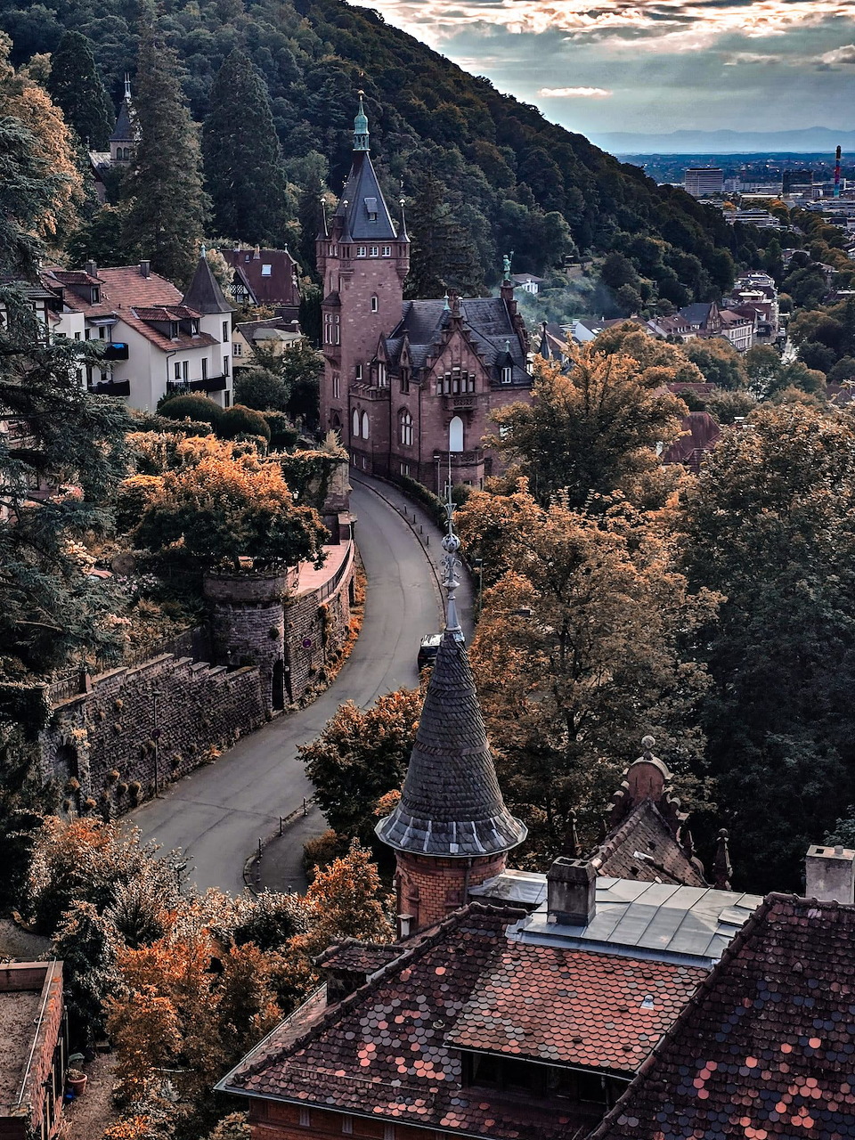 Aerial view of a historic castle tower in Heidelberg, Germany, with a winding road and autumn trees