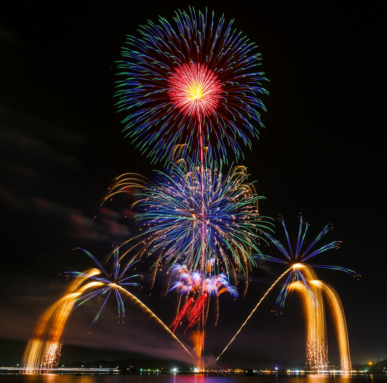 Colorful fireworks exploding over water with golden fountain sprays at night