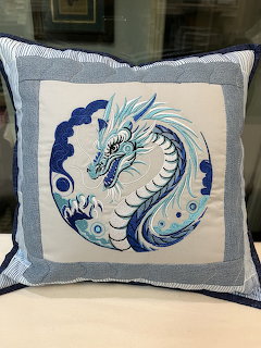 Decorative pilow with blue and white embroidered dragon in circular design on cream fabric with blue border