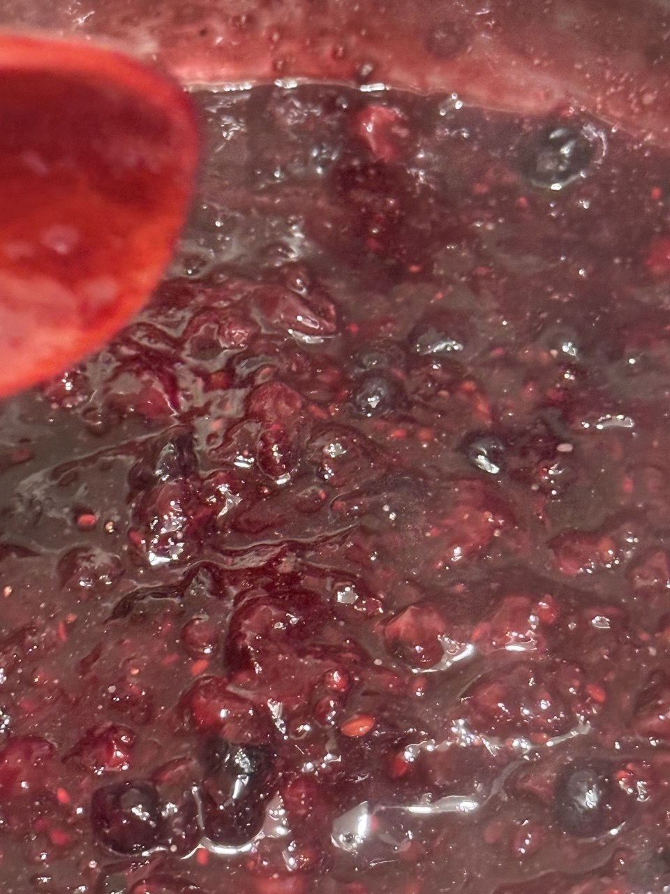 Close-up of red berry jam with fruit chunks and a red spoon