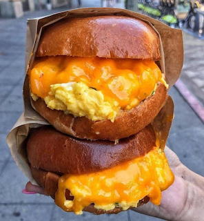 Two stacked breakfast sandwiches with eggs and melted cheese on toasted buns held in hand