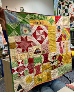 Colorful patchwork quilt with star blocks, trees, and house motifs held up for display