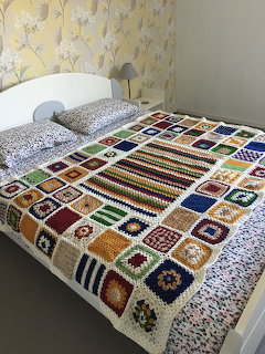 Bed with colorful crochet granny square blanket in a bedroom
