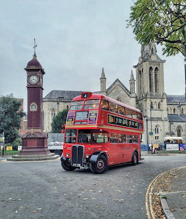 Vintage red double-decker bus near a church and clock tower at Highbury Barn