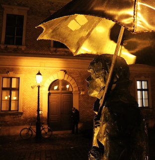 Bronze statue with umbrella at night in Budapest Óbuda square