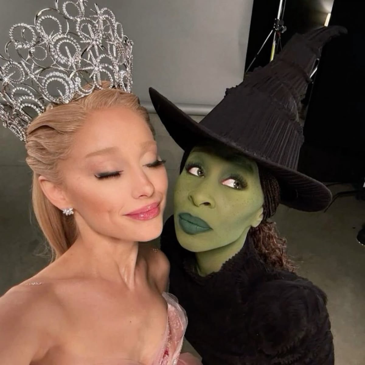 Two women dressed as Glinda and Elphaba pose together, one in a crown and one in a black witch hat.
