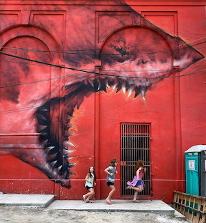 Large red shark mural on building wall with two people walking past on sidewalk