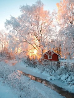 Red barn beside a narrow stream in a snowy winter landscape with frosted trees and soft sunlight